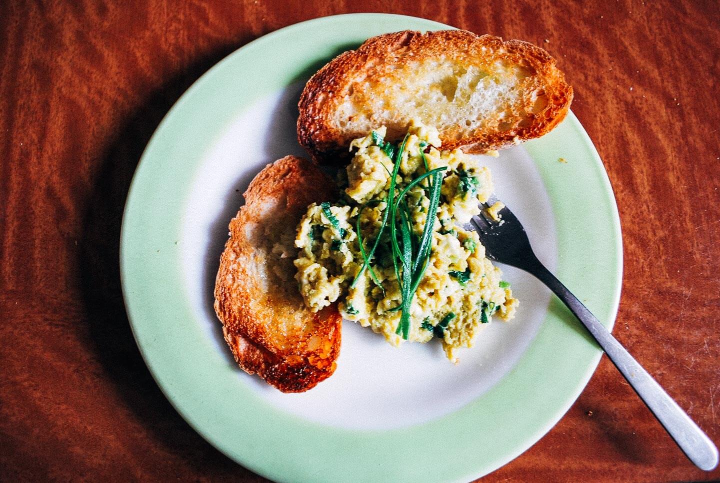 Slow-cooked scrambled eggs require patience, but reward the eater with exceptional flavor. These slow-cooked scrambled eggs are mixed with ricotta, Parmesan, garlic scapes, and spring onions, but feel free to add whatever cheese and alliums you may have on hand. 