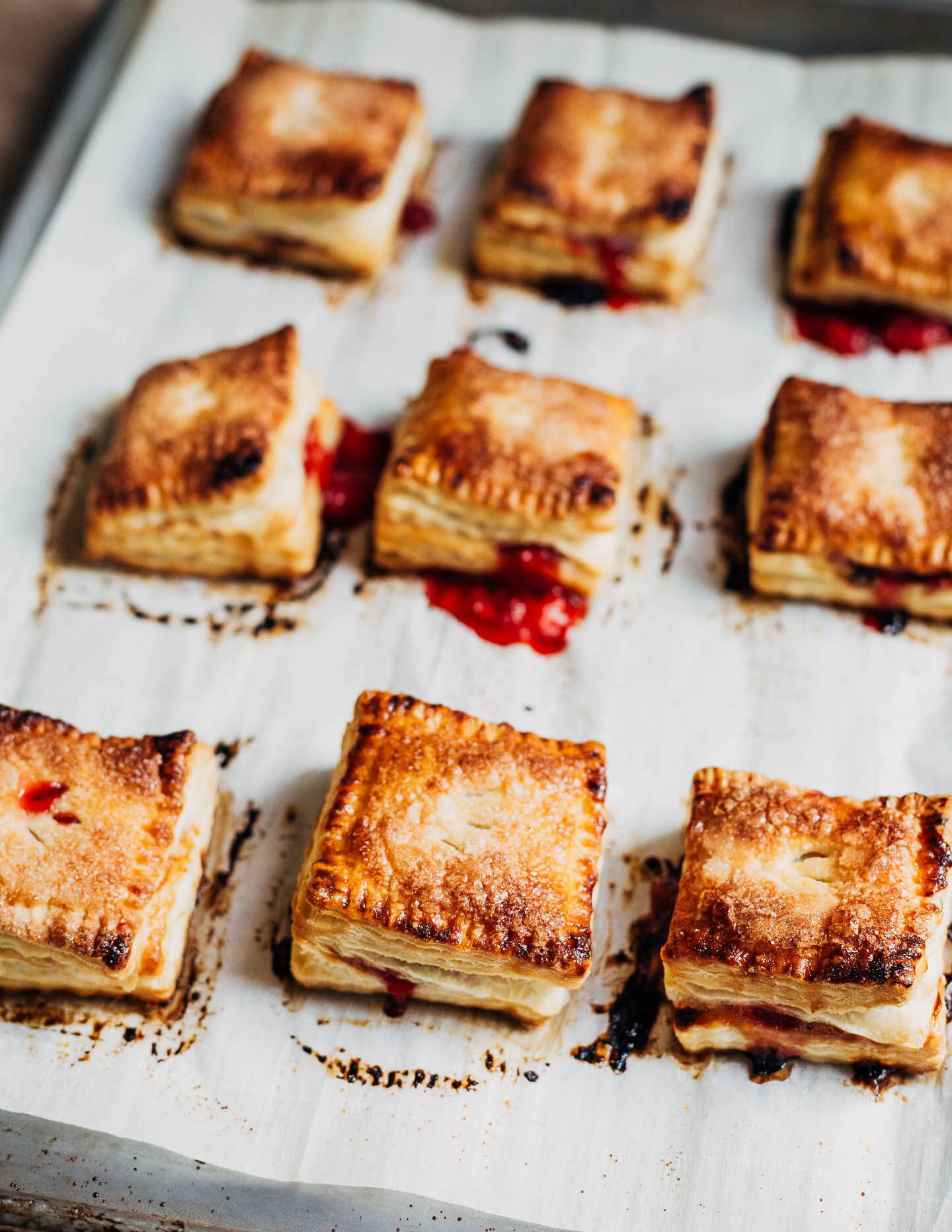 Nine strawberry basil hand pies, just out of the oven. The pies are seen from a 3/4 view and are a rich golden hue with a little bit of red strawberry juice oozing out. 