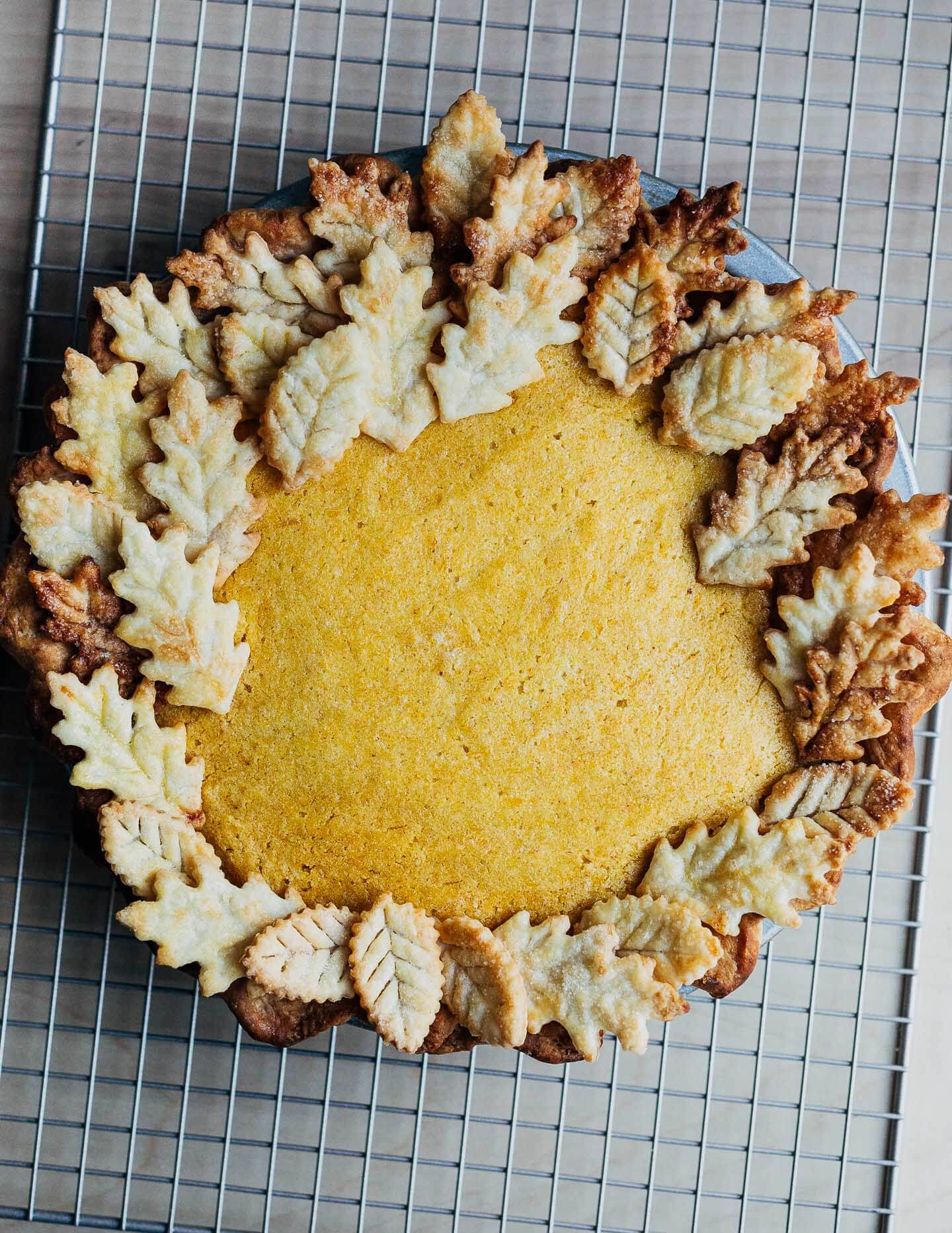 A pumpkin pie with a decorative leaf crust sitting on a baking rack