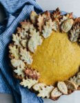 A pumpkin pie with a decorative leaf crust sitting on a table