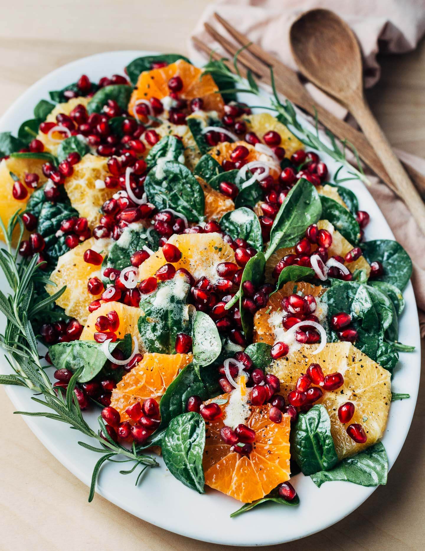 A platter with an orange and pomegranate salad with serving utensils alongside. 
