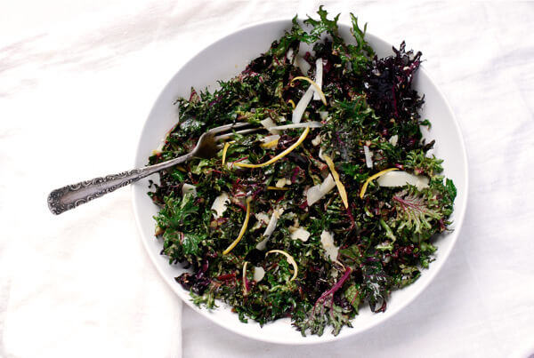 A bowl of kale salad with serving tongs. 