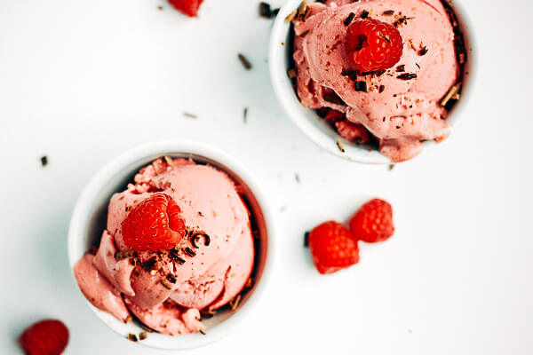 Two small bowls with raspberry frozen yogurt with a raspberry on top. 