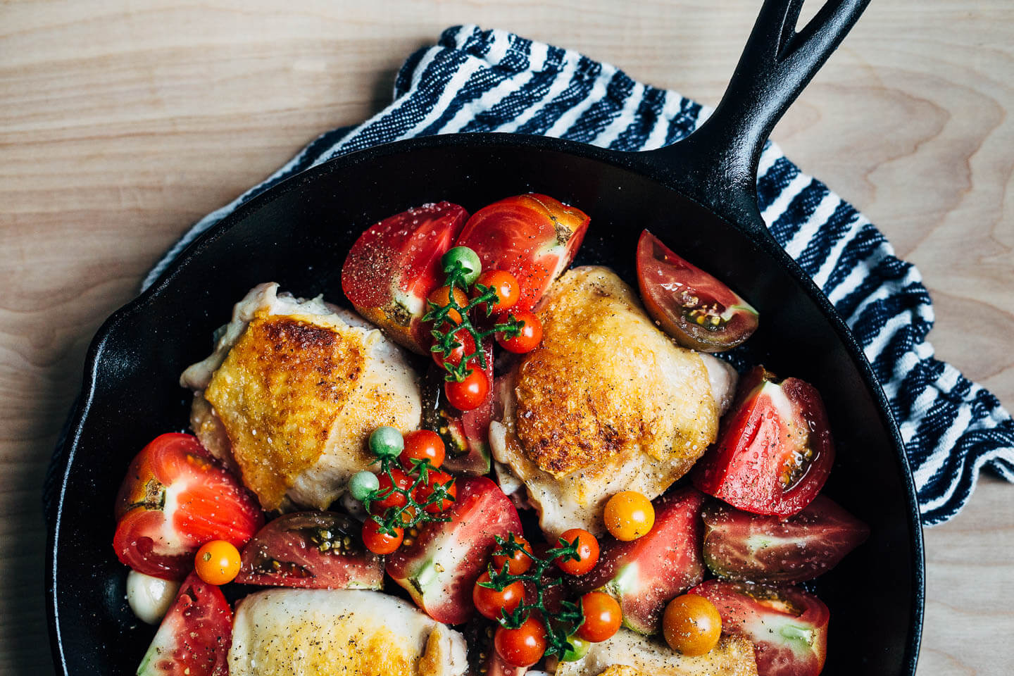 A overhead view of cast iron-seared chicken thighs with heirloom tomatoes tucked all around. 