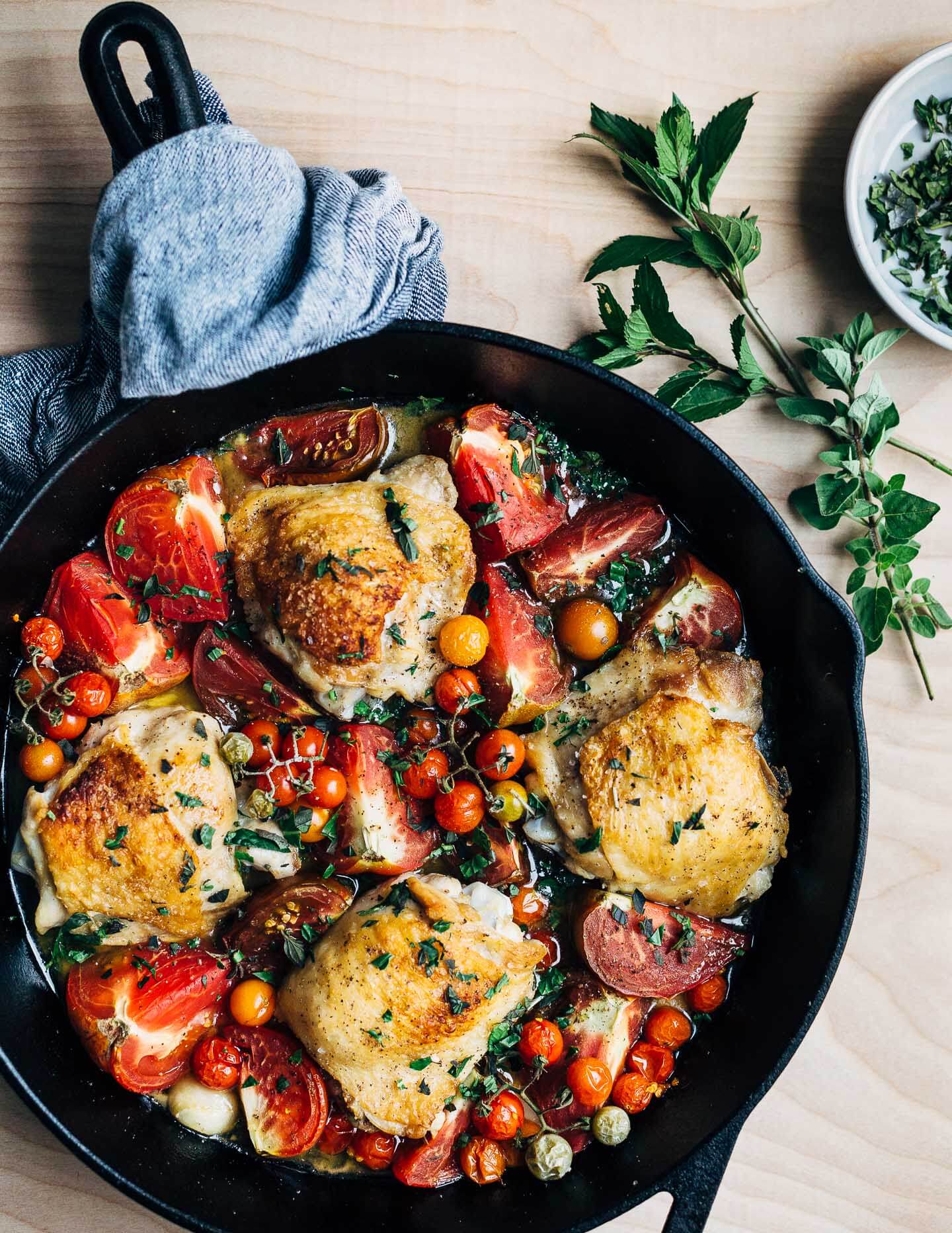 A cast iron skillet with golden chicken thighs and roasted tomatoes tucked all around. 