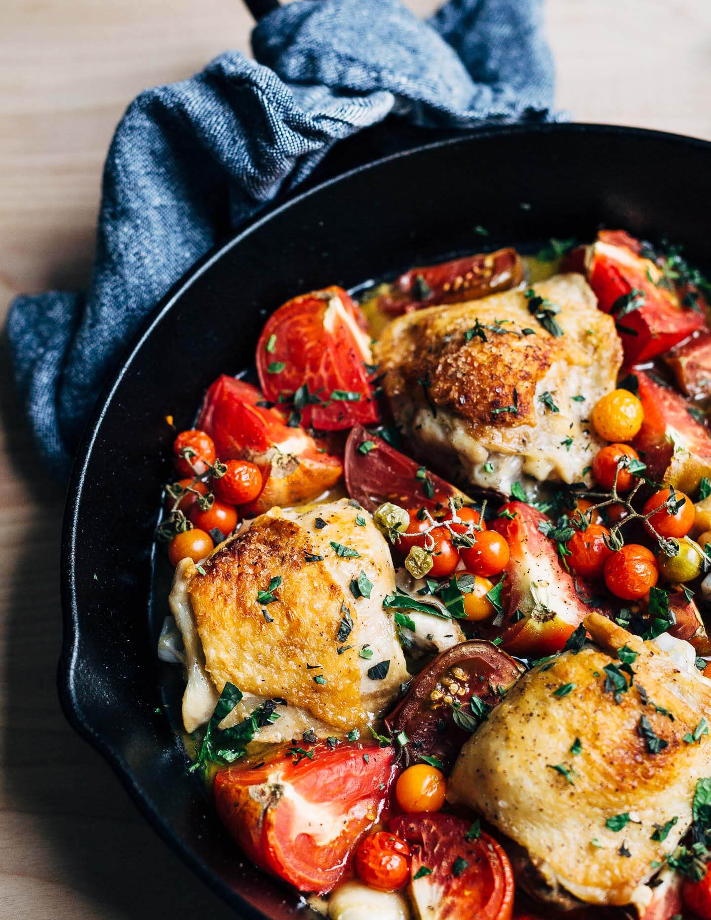A cast iron skillet with golden chicken and roasted tomatoes. 