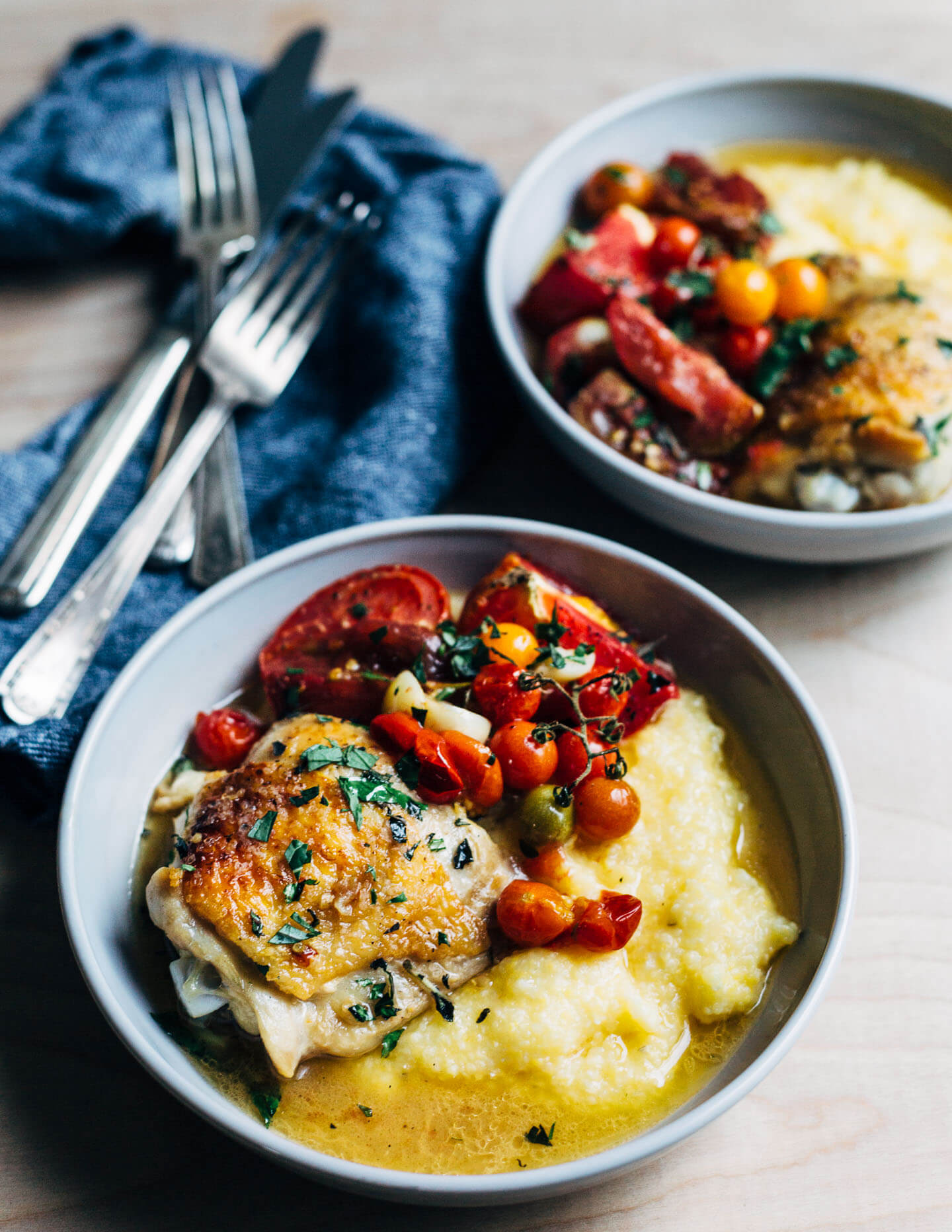 Bowls of baked chicken with tomatoes served over creamy polenta. 