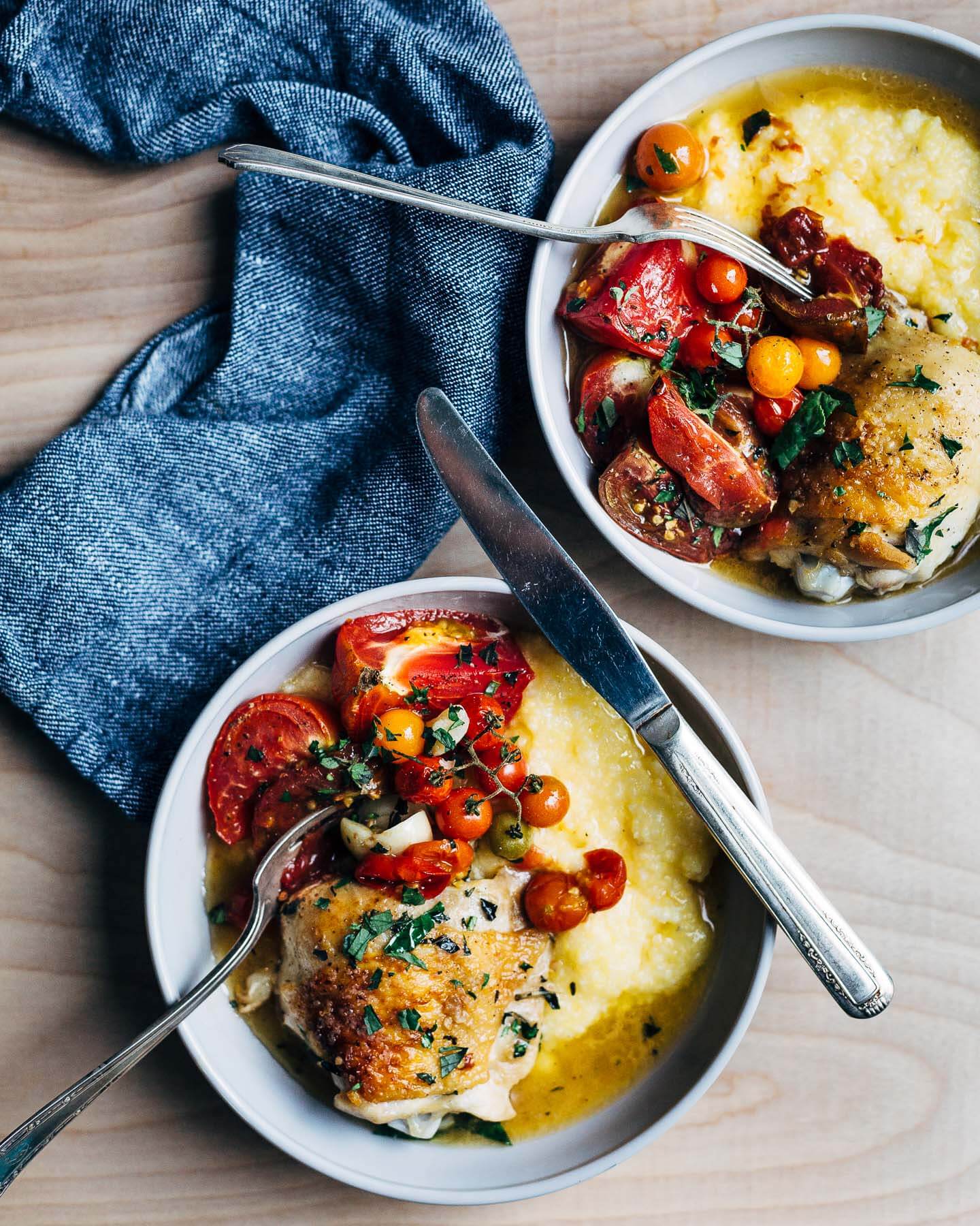 Two bowls of baked chicken with tomatoes served over creamy polenta. 