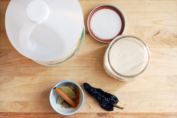 Looking down on a bottle of vinegar, a jar of sugar, with a dried chile, and cinnamon stick on the side. 