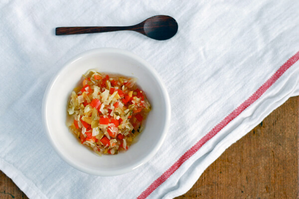 A small bowl of chowchow on a white napkin with a little spoon alongside. 