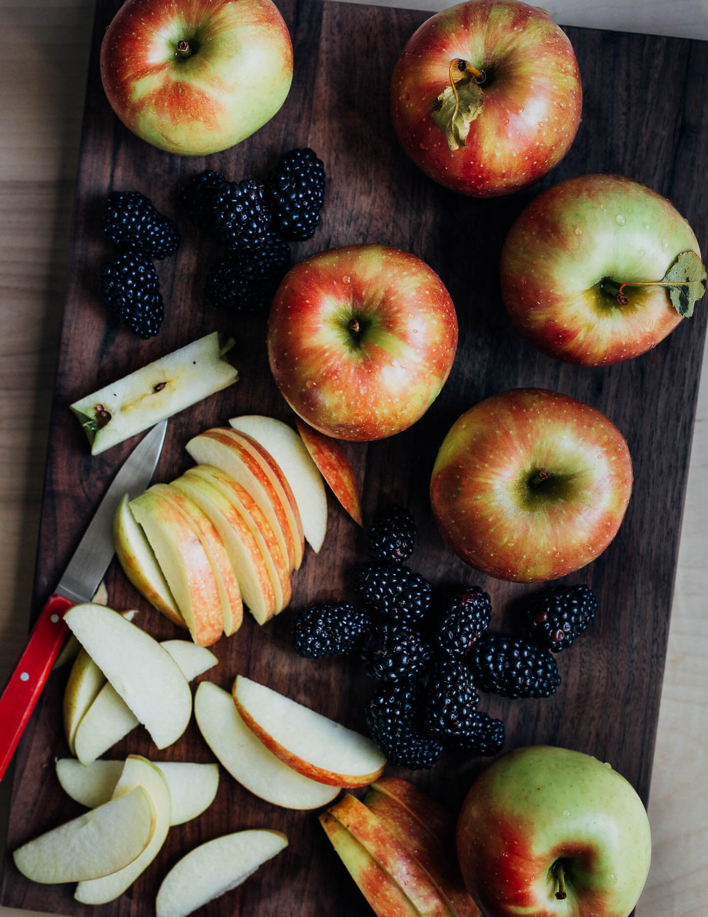 Whole and sliced apples and blackberries on a cutting board. 