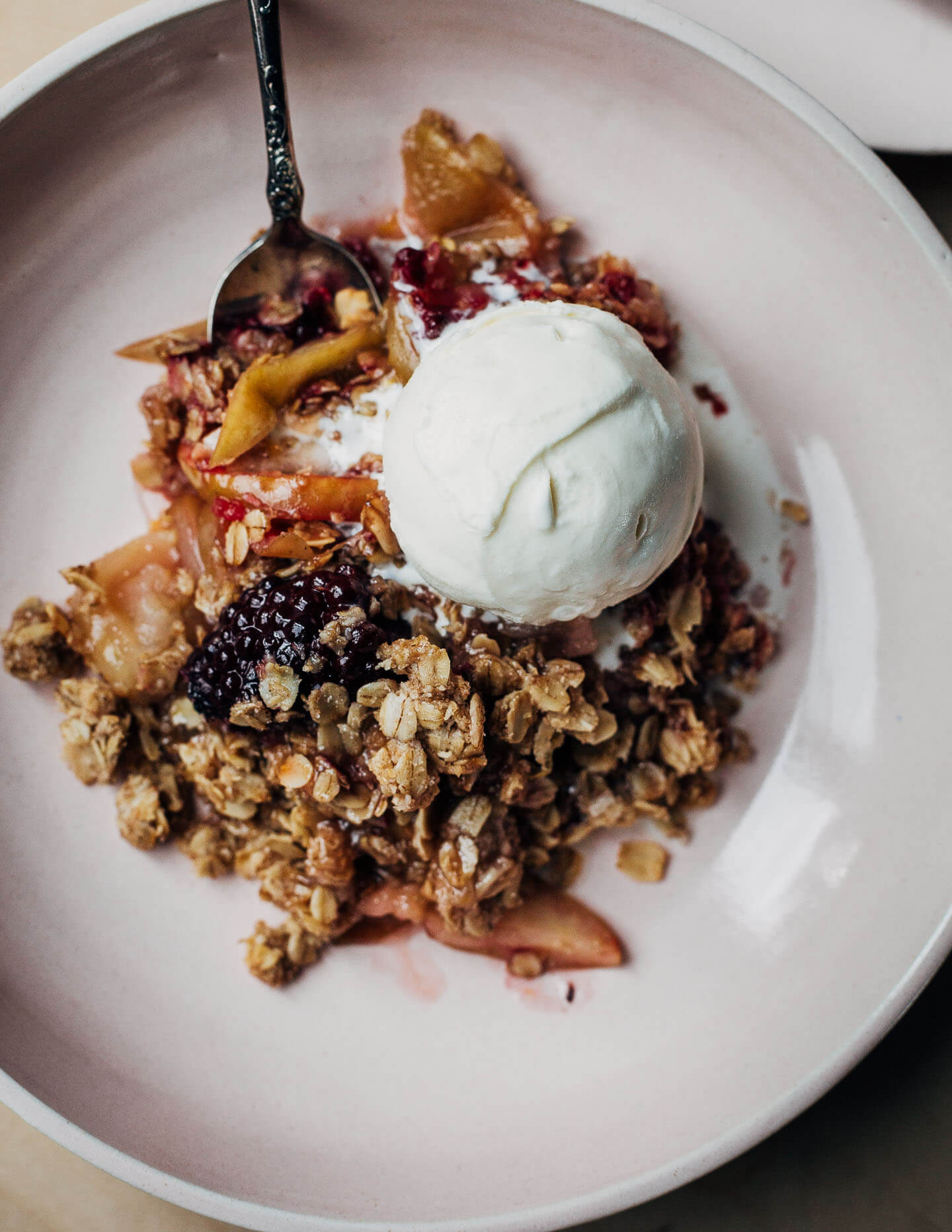 A pink bowl with a serving of crisp and a scoop of ice cream.