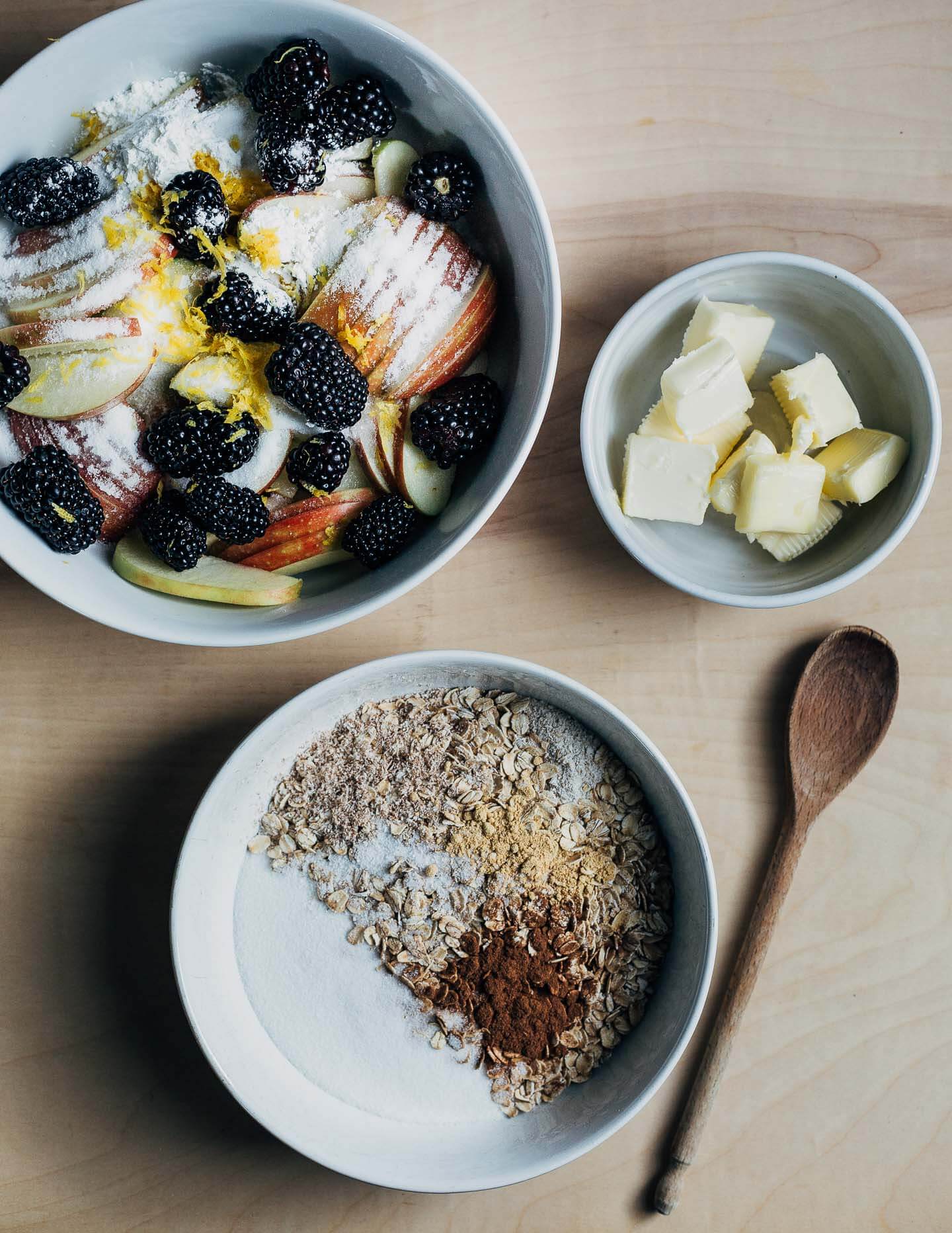 Bowls with crisp filling, crisp topping, and sliced butter on a table. 