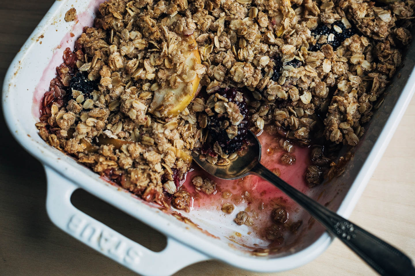 A crisp with a serving removed and a spoon in the baking dish. 