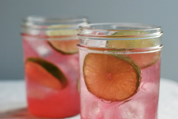 Two glasses with lime slices and concord syrup. 