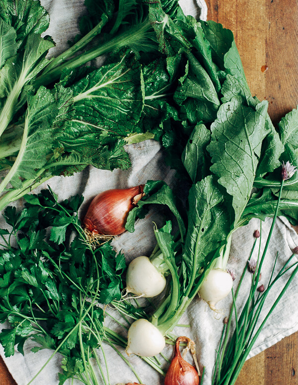 Turnips, shallots, chives, and greens laid out on a white cloth. 