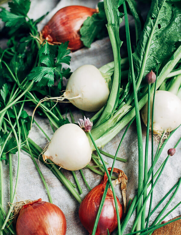 Turnips, shallots, chives, and greens laid out on a white cloth. 