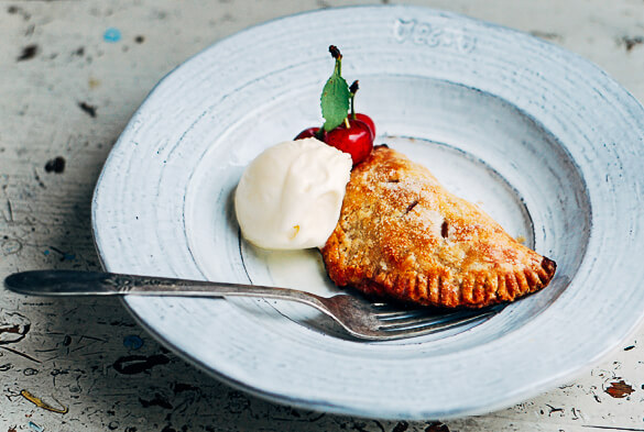 A hand pie in a bowl with a scoop of vanilla ice cream and fresh sour cherries for garnish. 