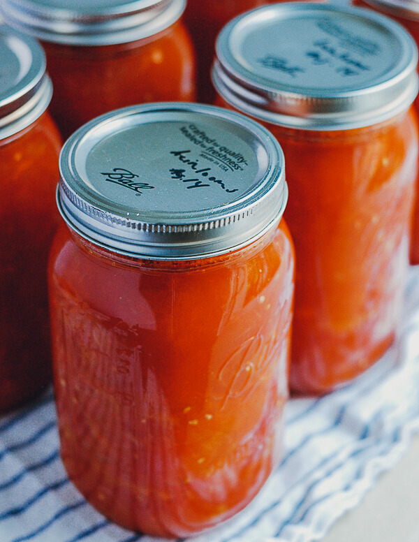 A jar of canned crushed tomatoes. The lids are labeled "heirlooms, Aug 14."