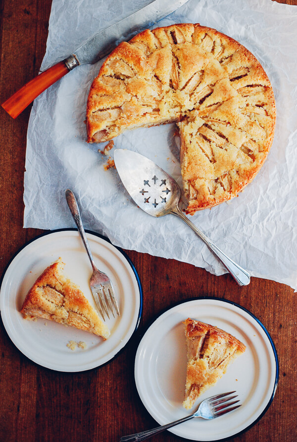 An apple cake next to two slices on little plates. 