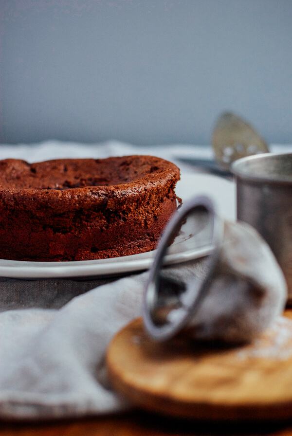 A sieve for powdered sugar in the foreground and a chocolate cake in the background. 