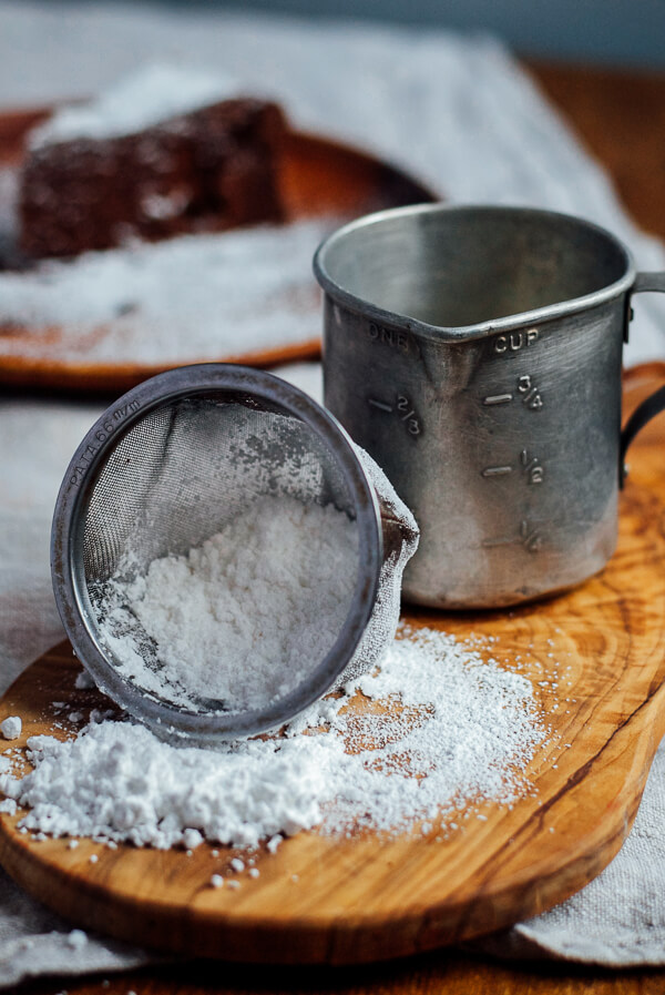 A sieve with powdered sugar and a measuring cup o a cutting board. 