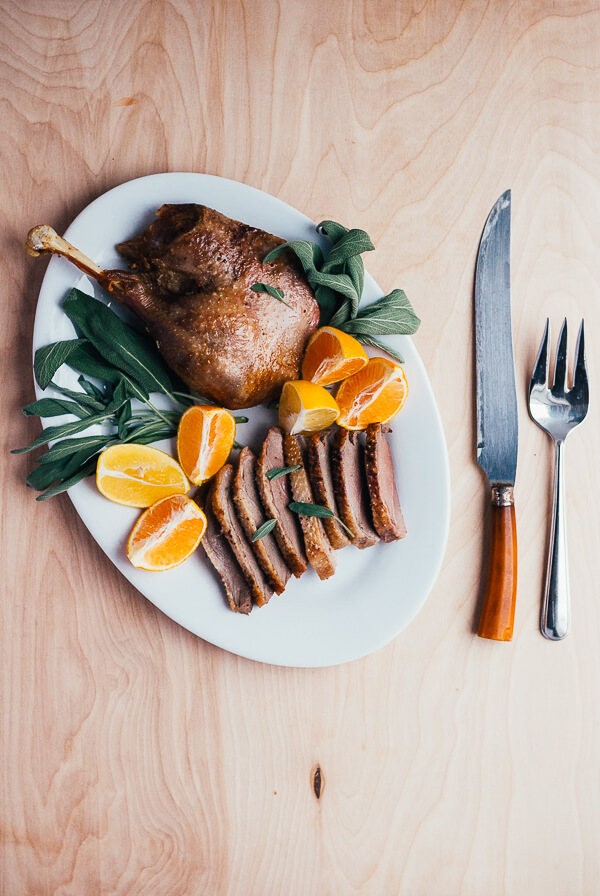 A carved roasted goose on a platter with sliced citrus. 