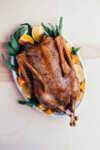 A roasted goose on a platter with sliced citrus.