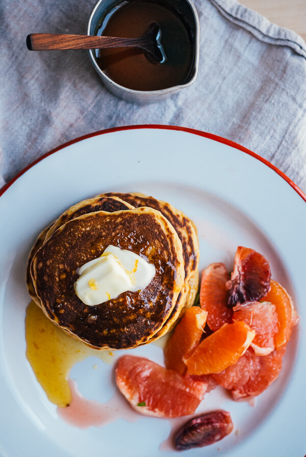 A plate of pancakes with syrup and an oange salad in the side. 