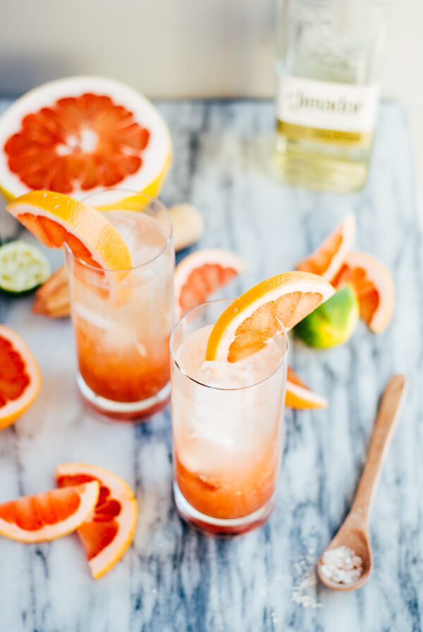 Two glasses of pomelo palama cocktails, with salt and citrus scattered around. 