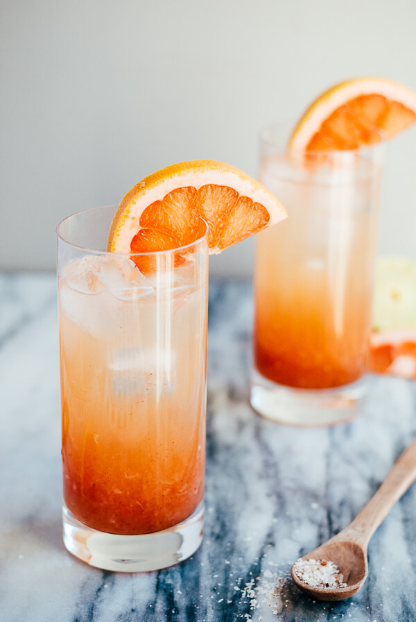 Two glasses of pomelo palama cocktails, with salt and citrus scattered around. 