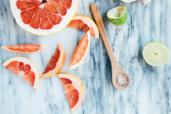 Sliced of pomelo, grapefruit, and lime scattered on a marble surface. 