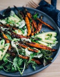 A platter with greens, roasted carrots, and avocados.