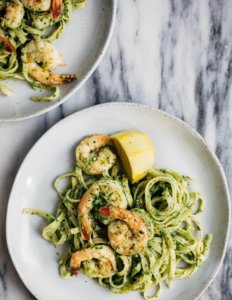 Two plates of linguine with pesto, shrimp, and lemon wedges