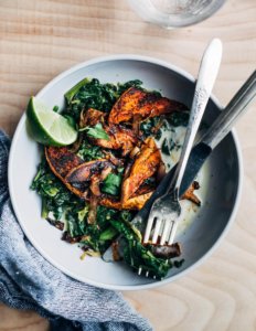 A bowl of greens with roasted sweet potatoes and a lime wedge