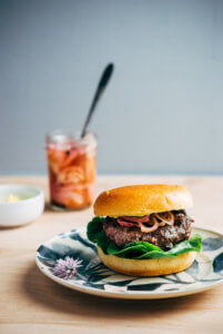 A burger on a plate with pickled shallots in the background.