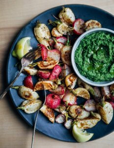A platter with roasted radishes and turnips and a bowl of pesto