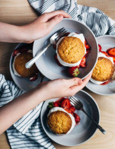 Two hands holds a bowl of strawberry shortcake, with other bowls of shortcake in the background.