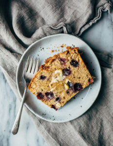 A slice of blueberry banana bread smeared with butter on a plate.