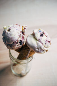 Two drippy ice scoops of blueberry ice cream cones in a glass jar.