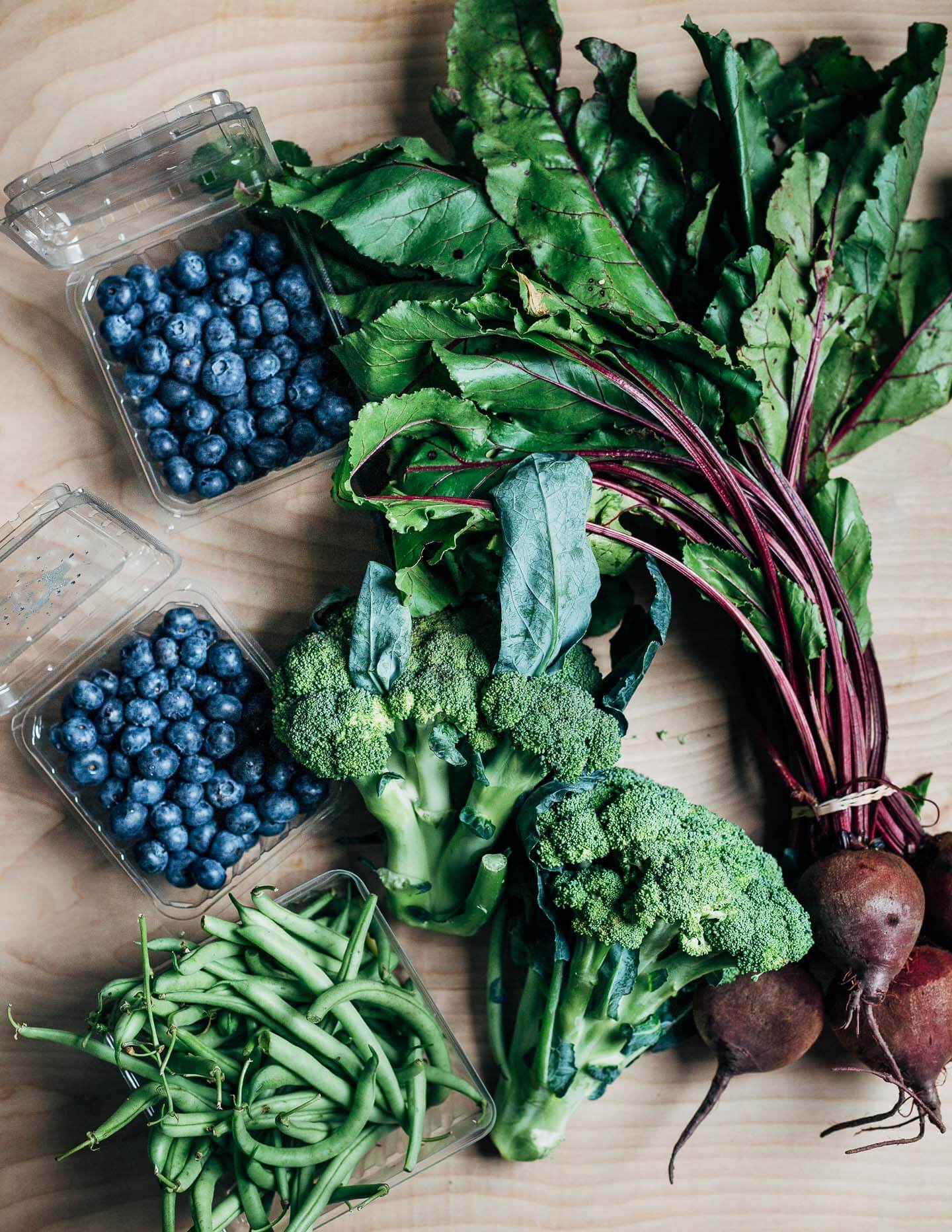 Blueberries, broccoli, beets, and green beans arranged on a table. 