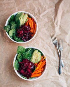 Two bowls with greens, pickles, and carrots.