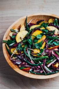A big wooden bowl filled with a green bean, red cabbage, and peach salad.