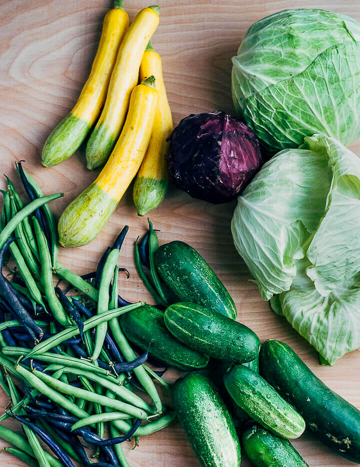 An assortment of produe laid out, with summer squash, green beans, cabbage, and cucumbers.