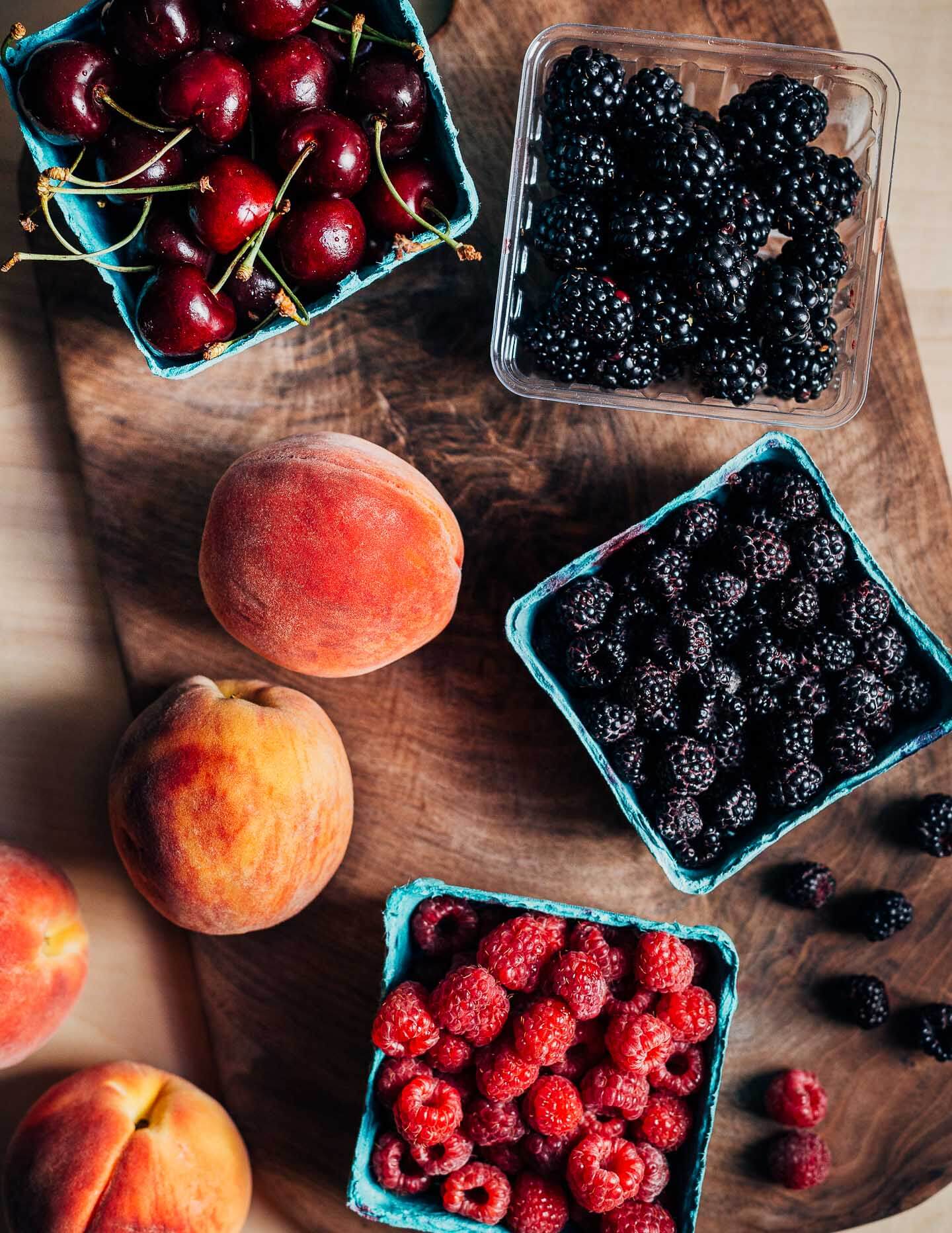 Little fruit holders with blackberries, black raspberries, cherries, and red raspberries. 
