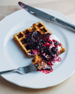 A plate with a cornmeal waffle and blackberry topping.