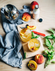 Two cocktails glasses surrounded by herbs and peaches