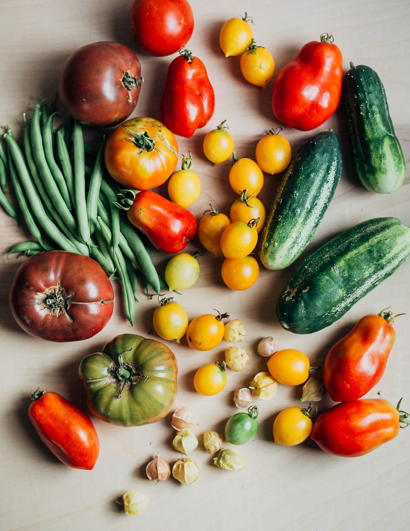 An array of summer produce with tomatoes, cucumbers, and green beans. 