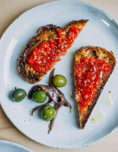 Toast with tomato pulp, with olives and anchovies on the side.