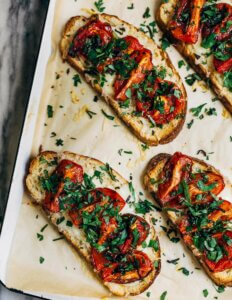 Toasts on a baking sheet with roasted tomatoes and herbs